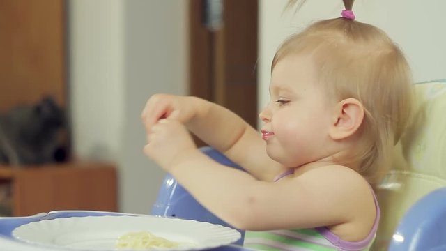Charming little girl eating spaghetti with her fingers and enjoying it