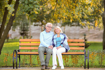 Cute elderly couple sitting on bench in autumn park