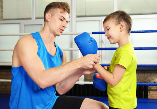 Trainer helping little boy put on boxing gloves in gym