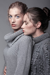 Two young women in gray sweaters on grey background. Beautiful girls stretching hands forward in embrace. Female friendship concept