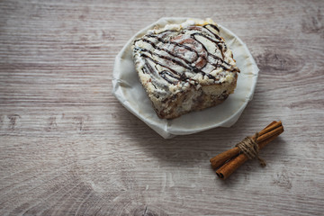 Still life of culinary spices and sweets. A sweet cake on a white porcelain plate with cinnamon sticks on a wooden surface in a cafe