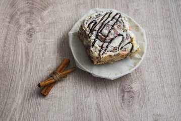 Still life of culinary spices and sweets. A sweet cake on a white porcelain plate with cinnamon sticks on a wooden surface in a cafe