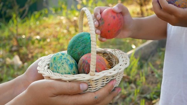 Close-up of woman hand holding a basket with easter eggs. Children put eggs into basket in sunshine background