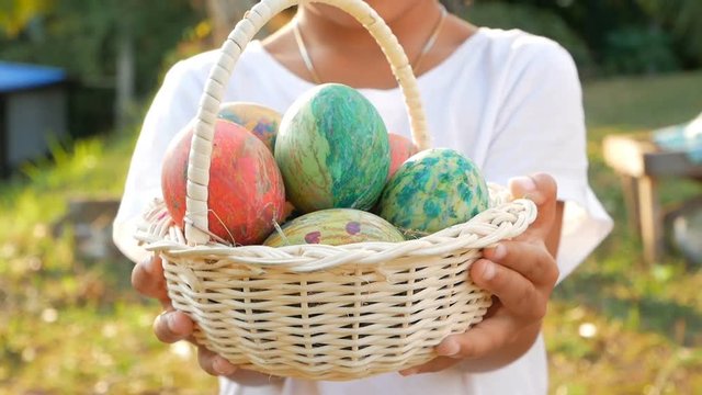 Close-up of children hand holding a basket with easter eggs in sunshine background