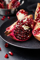 Fresh ripe pomegranate, cut into pieces on black concrete or stone background. Selective focus. Place for text.