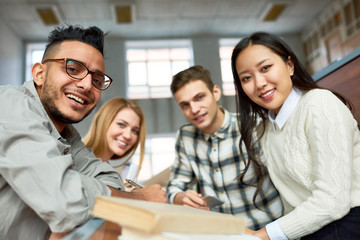 Multi-ethnic group of cheerful students looking at camera and smiling sitting at desk in lecture hall of modern college