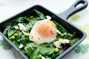 Closeup of poached egg with spinah, basil and feta in iron cast skillet. Soft focus.
