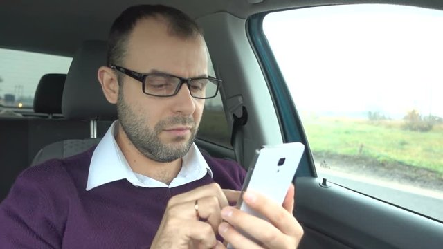 Businessman using a smartphone while sitting inside car. Man with a smart-phone in the  vehicle.
