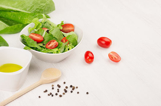 Healthy vegetarian spring salad -  fresh greens, tomatoes, pepper and olive oil on white wood background, closeup, copy space.