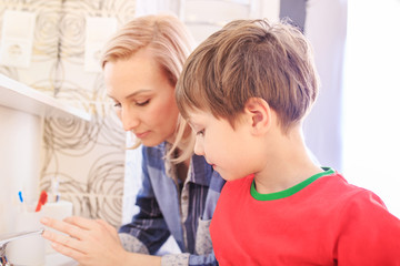 Obraz premium Beautiful happy mother and little son in bathrom brushing teeth together