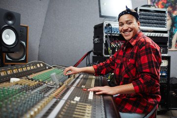 Young audio producer looking at camera while adjusting sound on special equipment