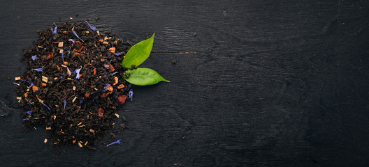 Black tea with flower petals of cornflower and dry berries. On a wooden background. Top view. Copy...