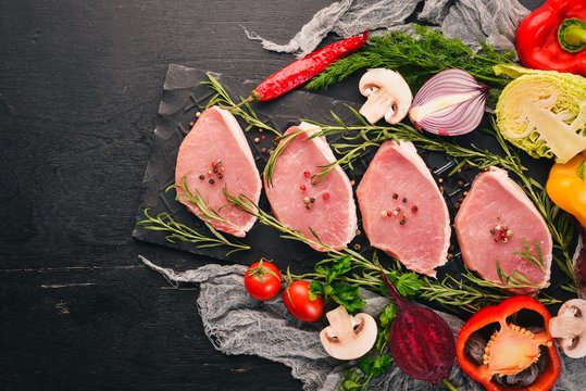 Beef steak with fresh vegetables and rosemary and spices on a black wooden background. Top view. Free space for text.