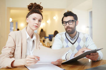 Young serious man and woman with documents looking at camera during meeting