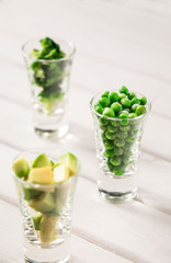 Assortment of green cut vegetables in shot glass on white background.