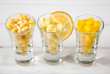 Assortment of yellow cut vegetables in shot glass on white background.