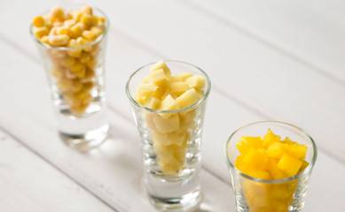 Assortment of yellow cut vegetables in shot glass on white background.