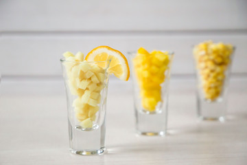 Assortment of yellow cut vegetables in shot glass on white background.