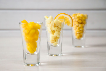 Assortment of yellow cut vegetables in shot glass on white background.