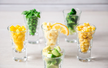 Assortment of yellow and green cut vegetables in shot glass on white background.