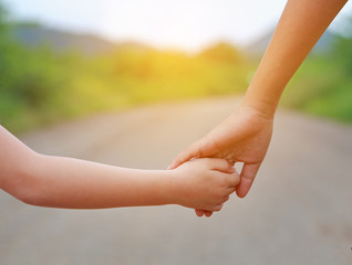Close up of Sister hold hands with small children walking on the road.