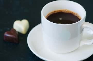 Cup of strong coffee and heart shaped dark and white chocolates on a black background.
