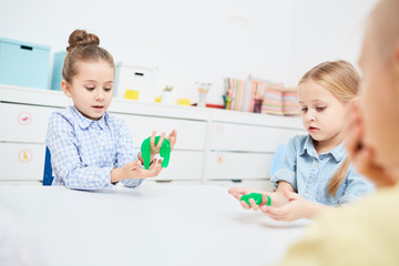 Little girls playing with green slime in kindergarten over table