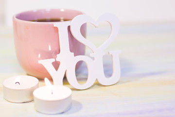 The concept of St. Valentine's Day, Love, Wedding, Anniversary. A romantic still life with coffee in a pink cup, I Love You inscription and two burning aroma candles, light blurred background