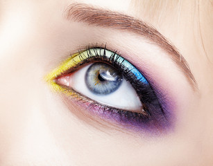 Closeup macro image of human female eye with violet, blue and and yellow makeup