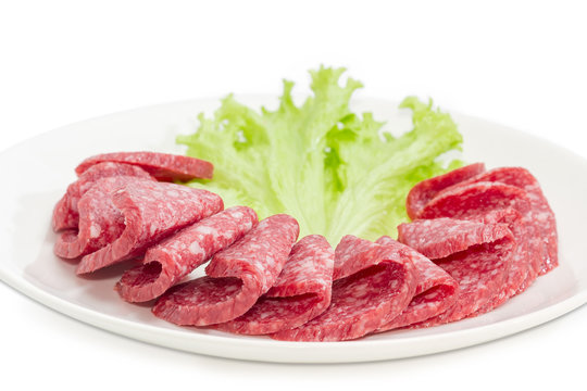 Sliced salami with lettuce leaf on a white dish closeup