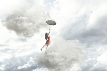 Surreal moment of an elegant woman flying in the middle of the clouds hanging on her umbrella