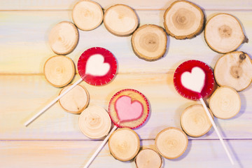 The concept of St. Valentine's Day, Love, Wedding, Anniversary with pink and red lolipops with hearts in a heart shaped frame of tree circles, colored wooden background, top view