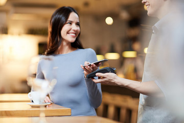 Modern girl with smartphone making contactless payment in cafe