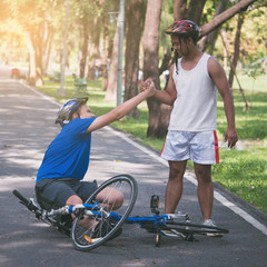 Fototapeta premium A young man helps his friend who get bicycle accident on a path.