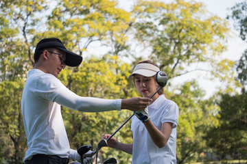 Asian young couple playing golf on golf course, the male partner is trainer to the female golfer