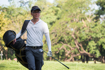 Portrait of asian young male golfer with golf club bag on the golf course.