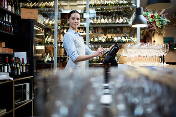 Young staff of restaurant standing by computer and entering data about latest orders and payments