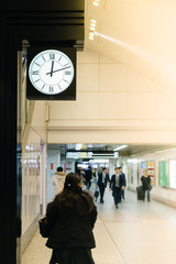 People walking at subway station for the train arriving with big clock time, background, Japan.