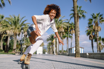 Black woman on roller skates rollerblading in beach promenade with palm trees - obrazy, fototapety, plakaty