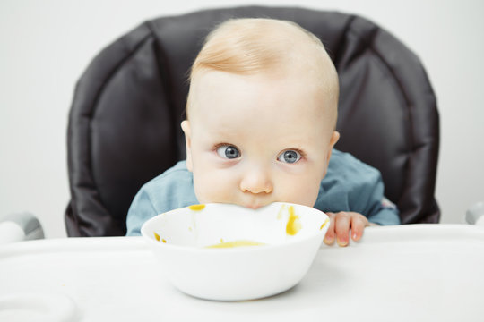 Cute baby has fun and bites board of bowl