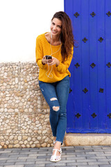 Full body cheerful female standing outside with earphones and mobile phone