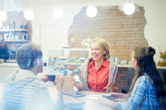 Laughing mature professional having tal kto her young colleagues during meeting in cafe