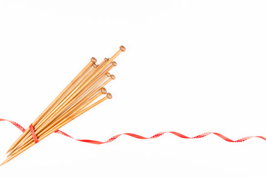 Wooden knitting needles and red and white polka dot ribbon on white background as frame