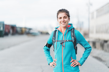 Obraz premium Portrait of young sporty woman with running backpack and listening music in industrial area