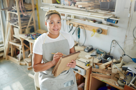 Young professional carpenter making notes in notepad while sitting in workshop