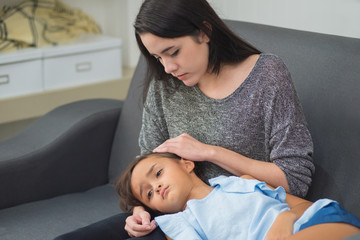 Young mother checking temperature of her sick little daughter on the couch