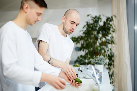Two young gay men washing avocado in the kitchen at home