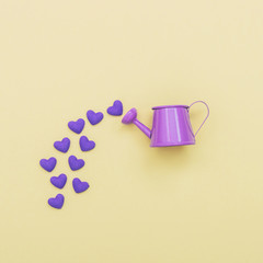 purple watering can flowers pouring hearts on a yellow background © EkaterinaChebotareva