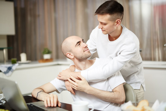 Young homosexual lovers looking at one another in embrace at home