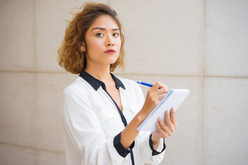 Serious Young Asian Woman Writing in Notebook